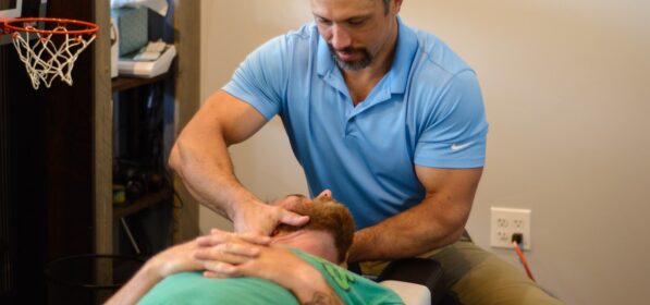 Chiropractor performing lower cervical spine adjustment on male patient in supine position